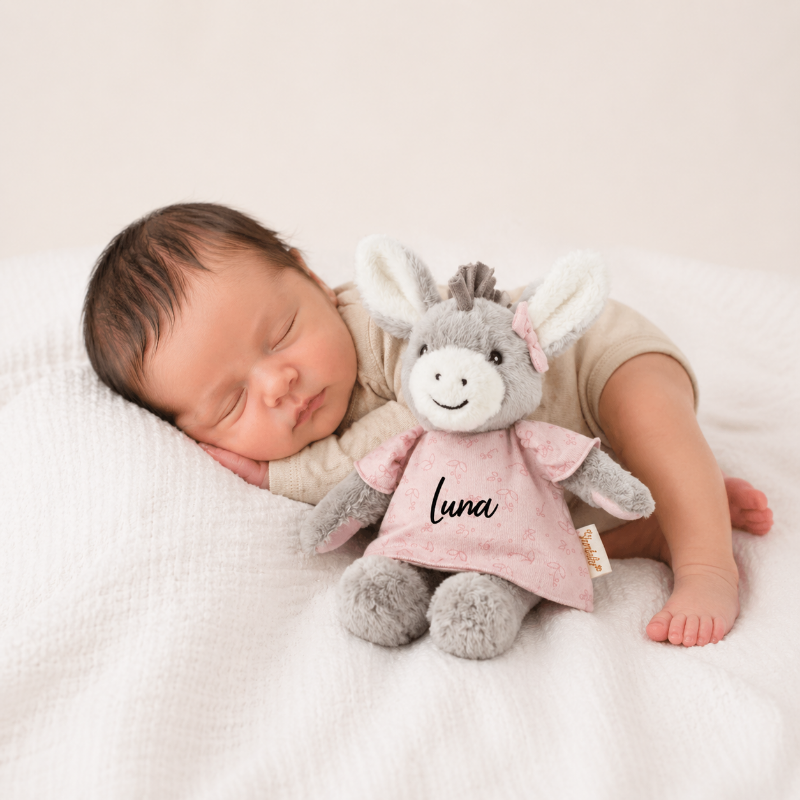 Neugeborenes Baby schläft auf einer weichen Decke neben einem personalisierten Kuscheltier Esel mit dem Namen Luna