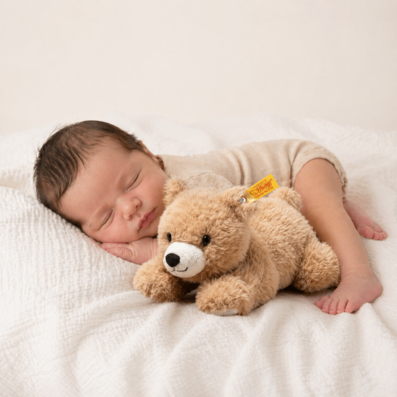 Neugeborenes Baby schläft auf einer weichen Decke neben einem beigen Teddybär Kuscheltier