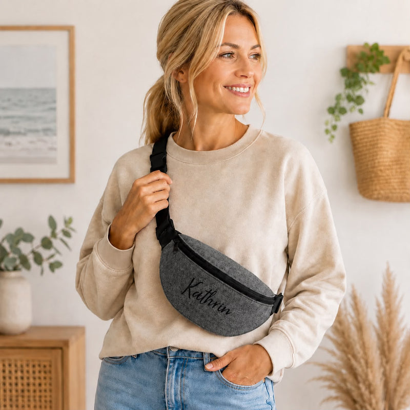 Frau trägt eine dunkelgraue Bauchtasche aus Filz mit schwarzem Reißverschluss und der Personalisierung Kathrin.
