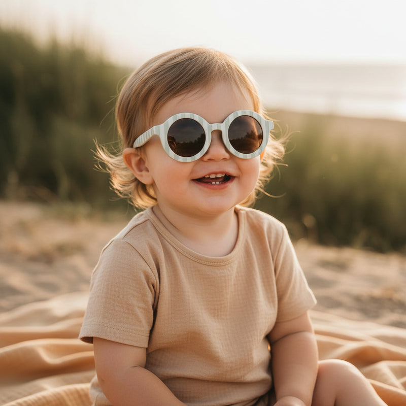 Kindersonnenbrille rund mit UV Schutz – Baby sitzt am Strand mit Sonnenbrille